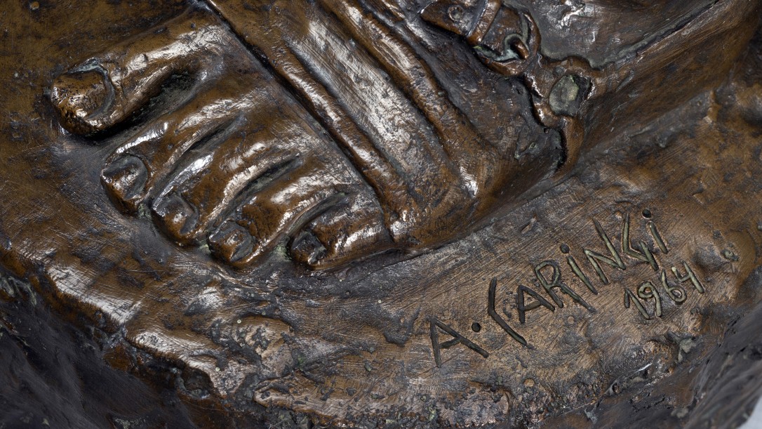 Escultura em bronze representando o "gaúcho laçador".  Figura masculina, em pé, apoiada sobre a perna esquerda, corpo e cabeça virada para frente. A cabeça, com cabelos na altura do pescoço, possui uma faixa amarrada na testa, barba e bigode.